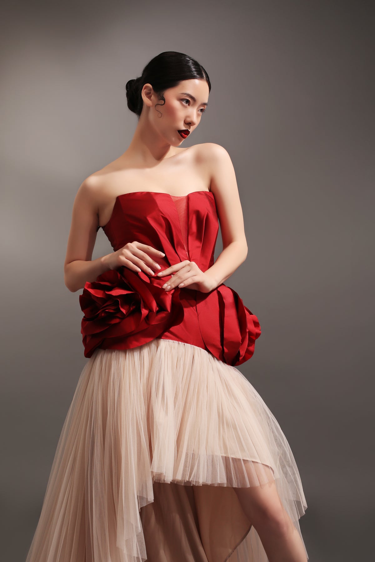 Red dress in deep v-neck cut with petals draping on hips with micro-pleated mullet skirt