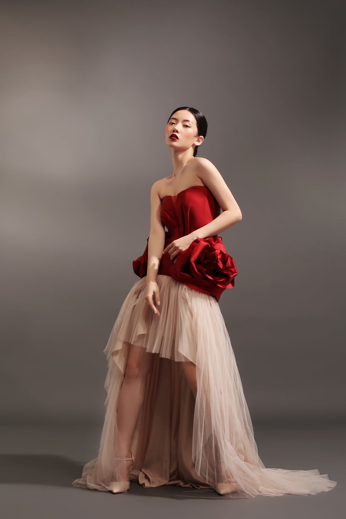 Red dress in deep v-neck cut with petals draping on hips with micro-pleated mullet skirt